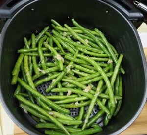 Seasoned green beans in the air fryer basket.
